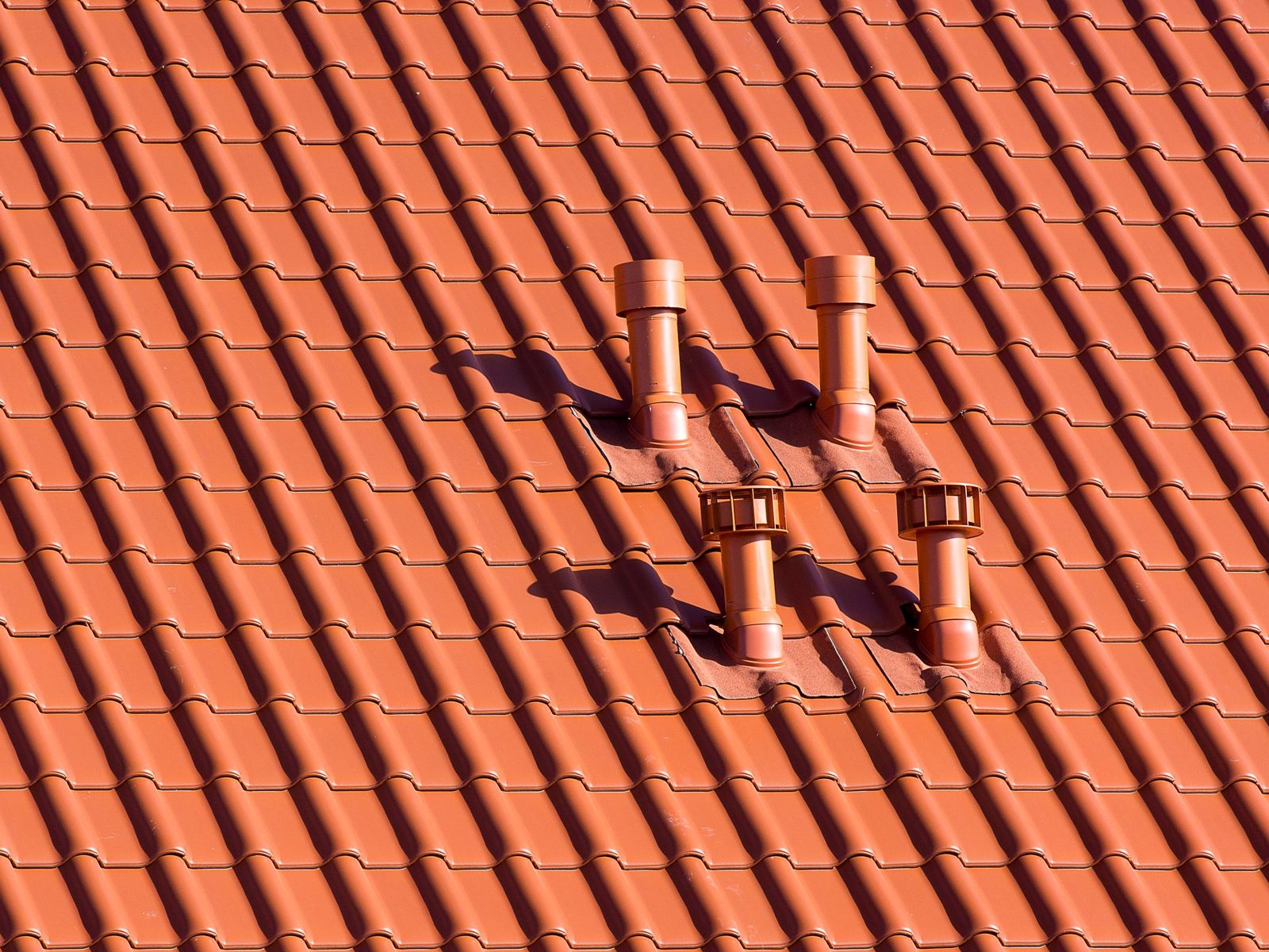 Orange clay roof tiles with four vent pipes coming through