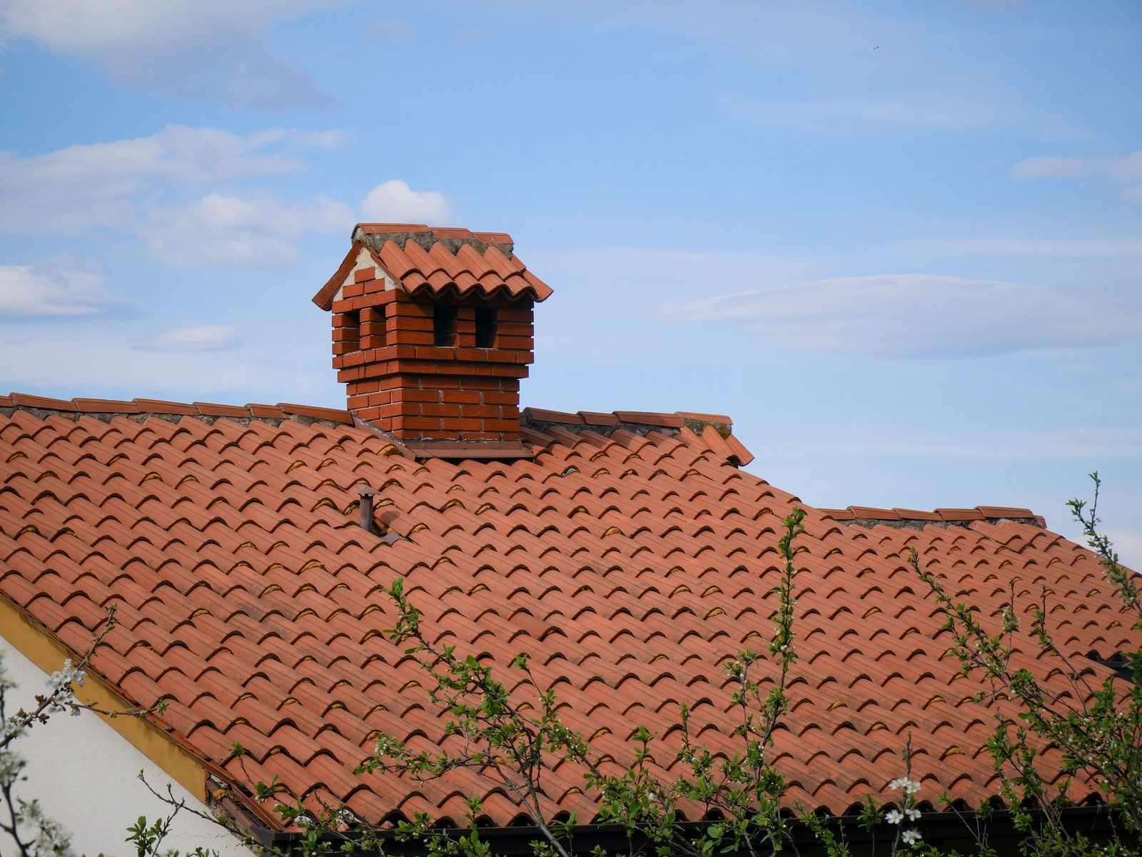Brick chimney with a tiled cap on a clay tile roof under a blue sky